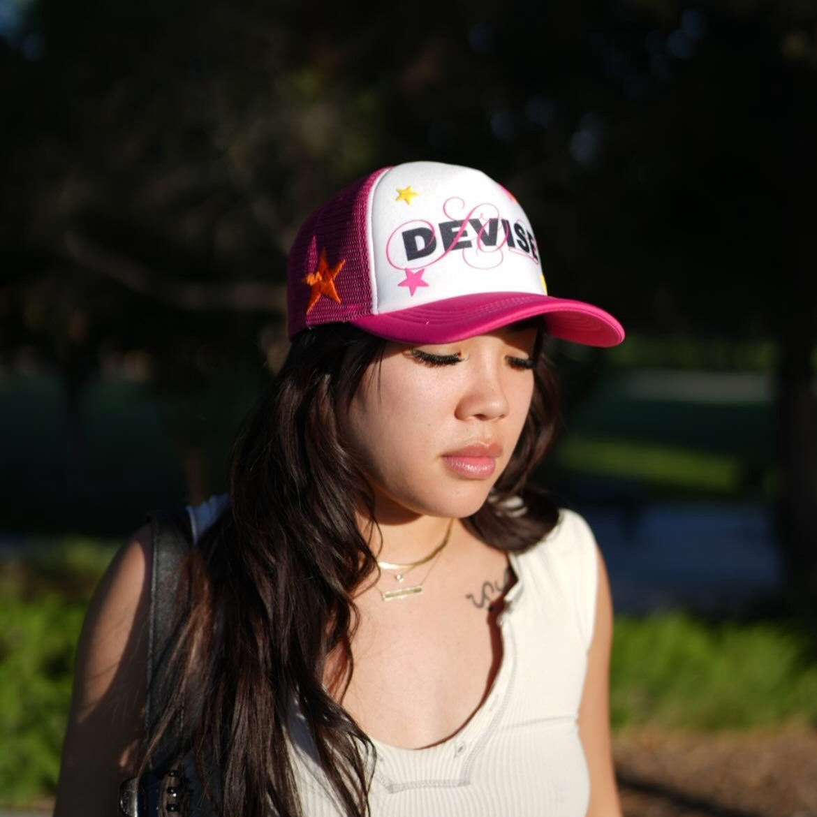 Woman wearing a white and pink cap with 'DEVISE' on it, standing outdoors.
